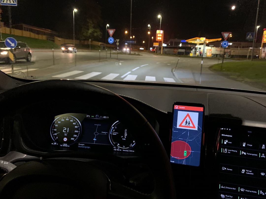 Foto som viser en mobilskjerm montert på dashbordet i en bil. Skjermen viser at bilen befinner seg i nærheten av en skole og at fartsgrensen er lav.