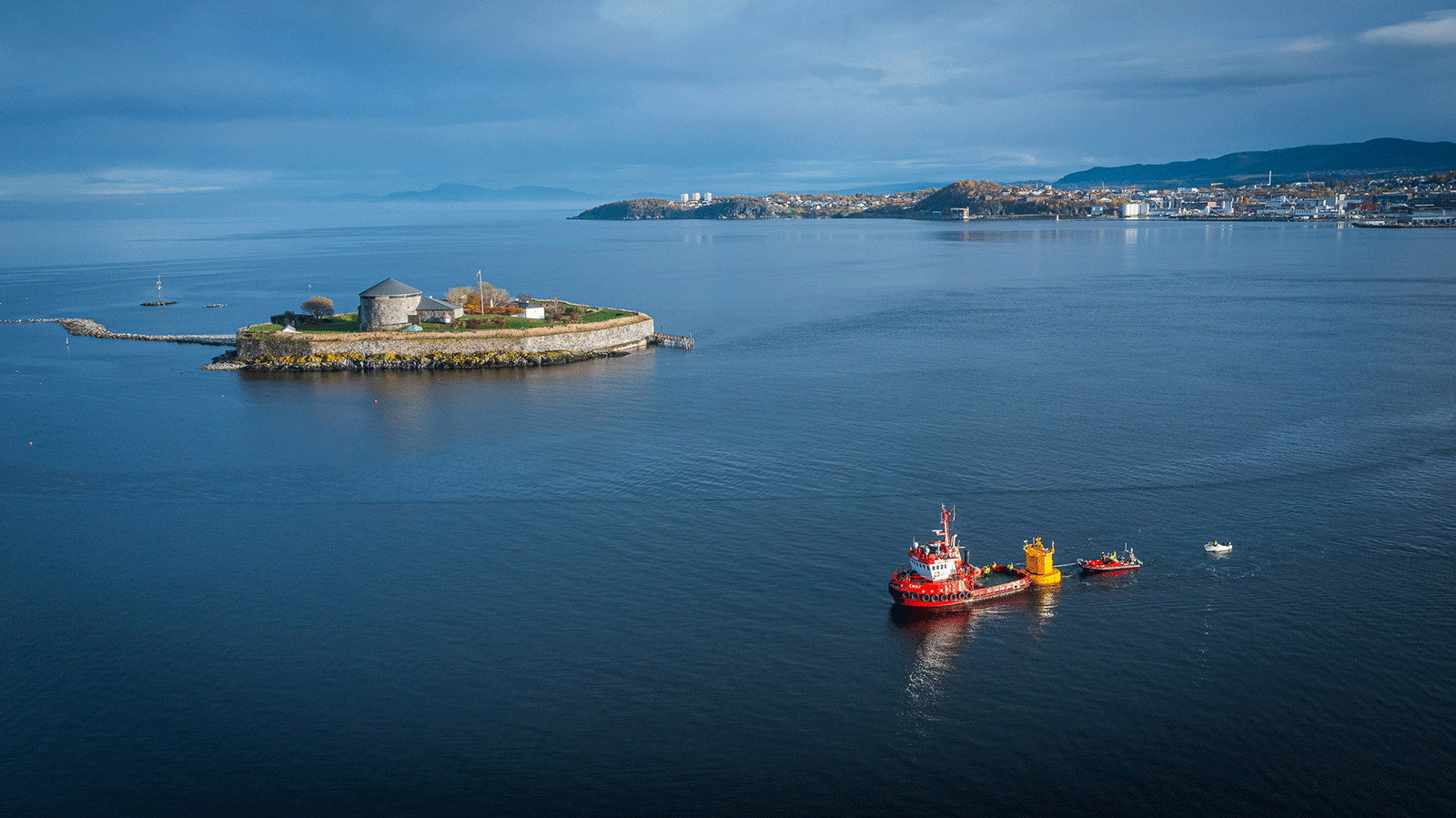Trondheimsfjorden med munkholmen og en båt som sleper ut bøya