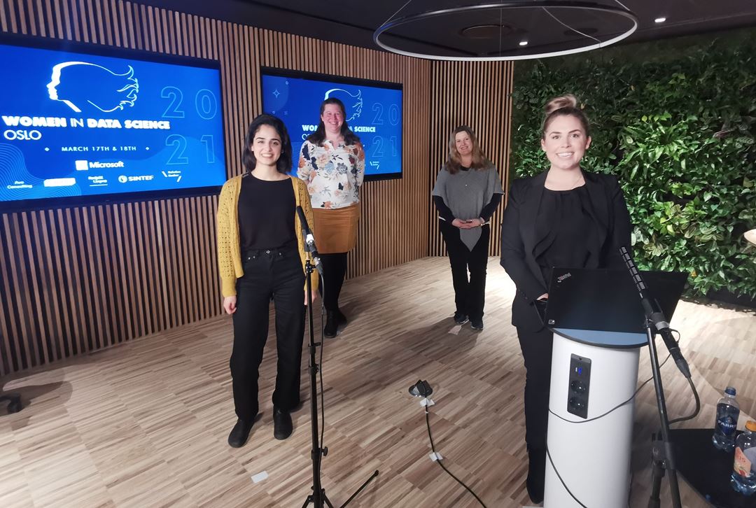 Fire kvinner foran mikrofoner og en skjerm med påskriften Women in Data Science