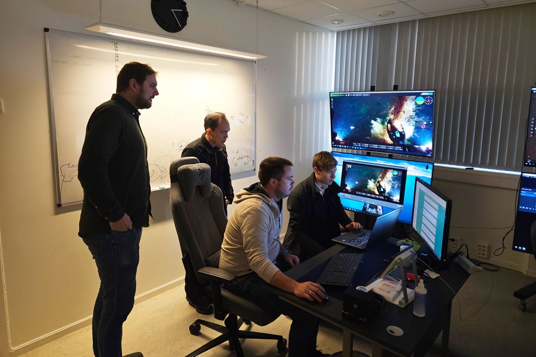 Four men gathered around computer screens