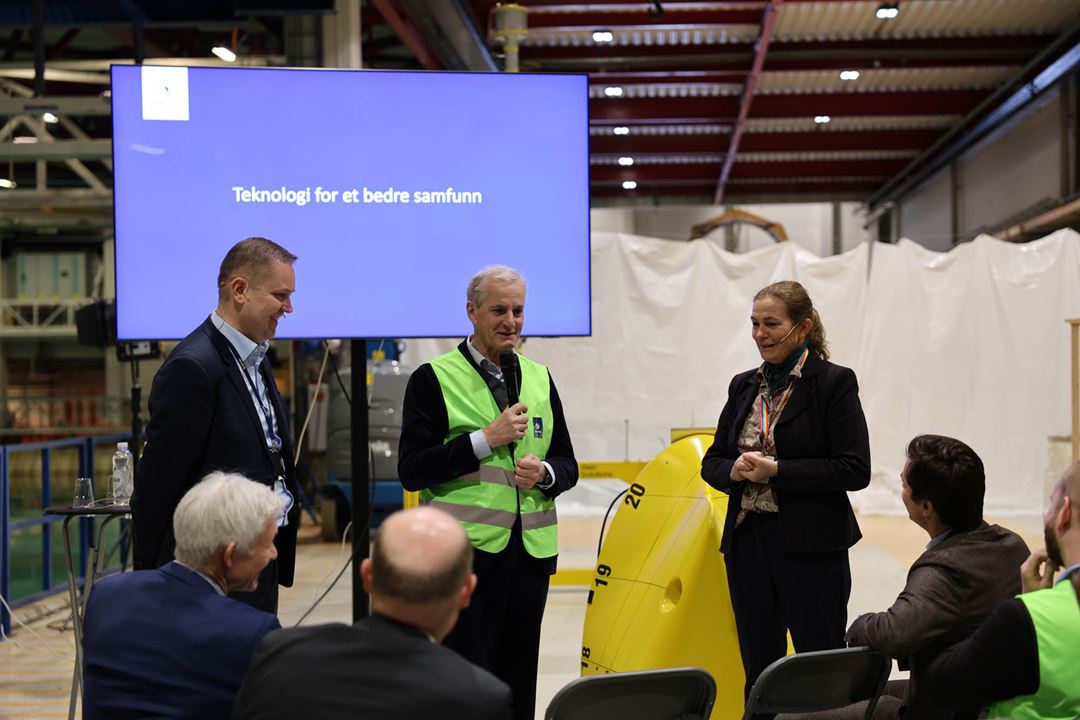 Tre personer presenterer foran en blå skjerm.