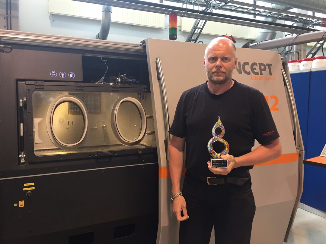 Seniorforsker Klas Boivie med spesialutmerkelsen "Additive Manufacturing Connection Point" fra ASTM International, foran metall AM-maskinen i Trondheim. Foto: SINTEF Raufoss Manufacturing