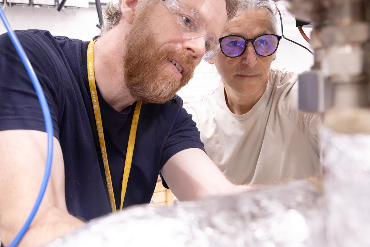 Two scientists wearing protective glasses and working on a technical piece of equipment.