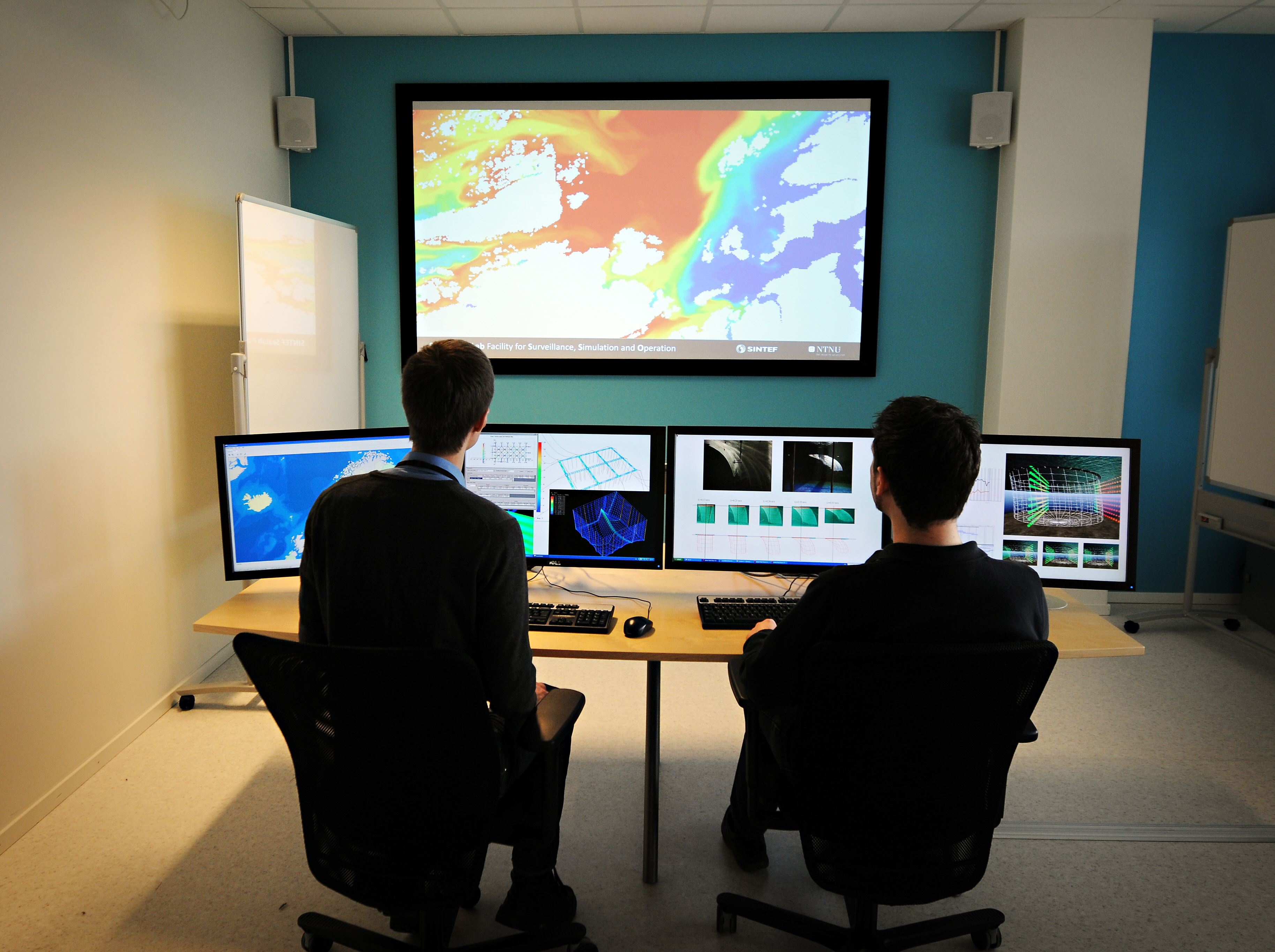 two people in front of several screens