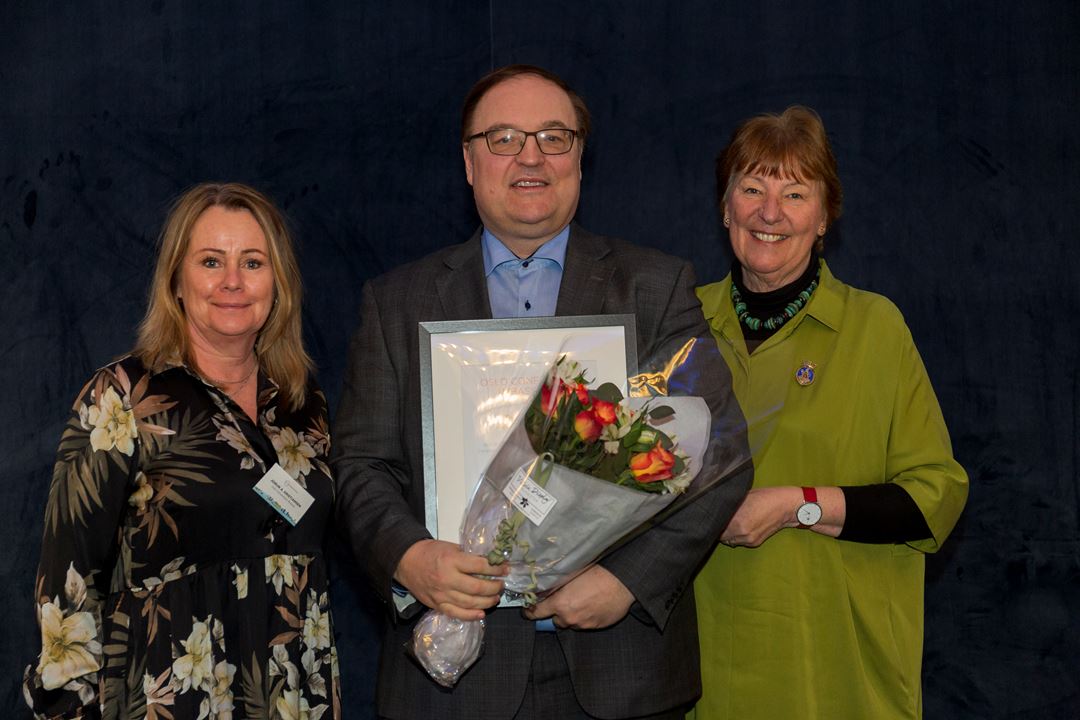 En mann som holder blomster og diplom, sammen med to kvinner