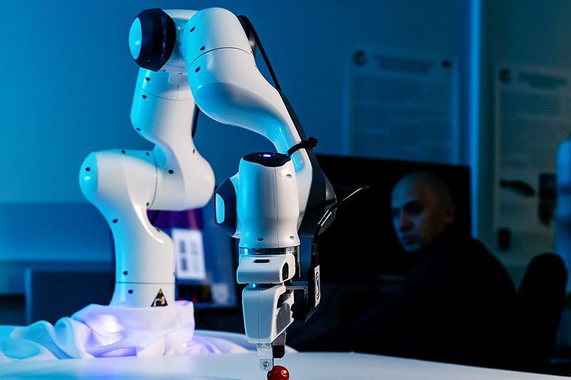 Robot som griper et eple. Person i bakgrunn