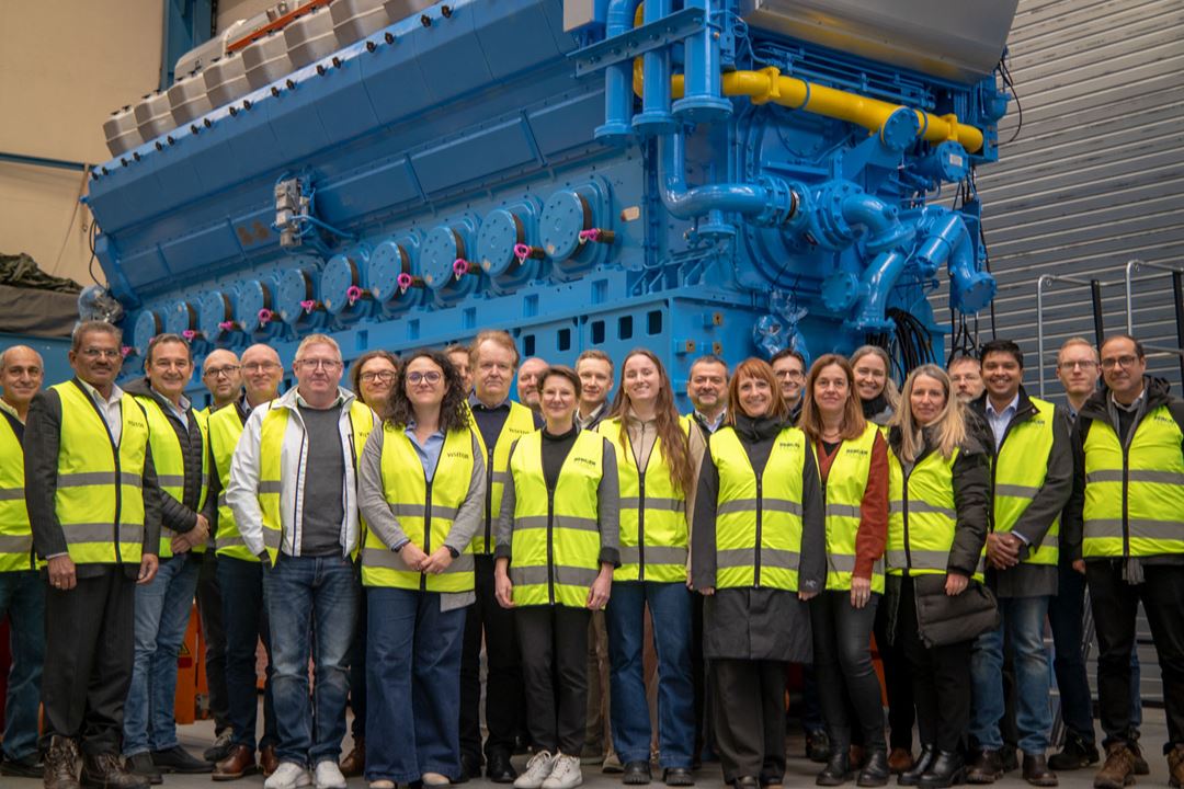 Group photo of people with yellow vests in front of a huge, blue engine.