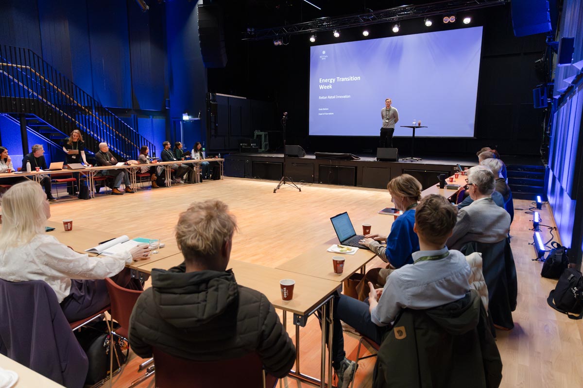 People attending a workshop, with someone holding a presentation on stage / Folk som deltar i en workshop, med en person som holder en presentasjon på en scene.