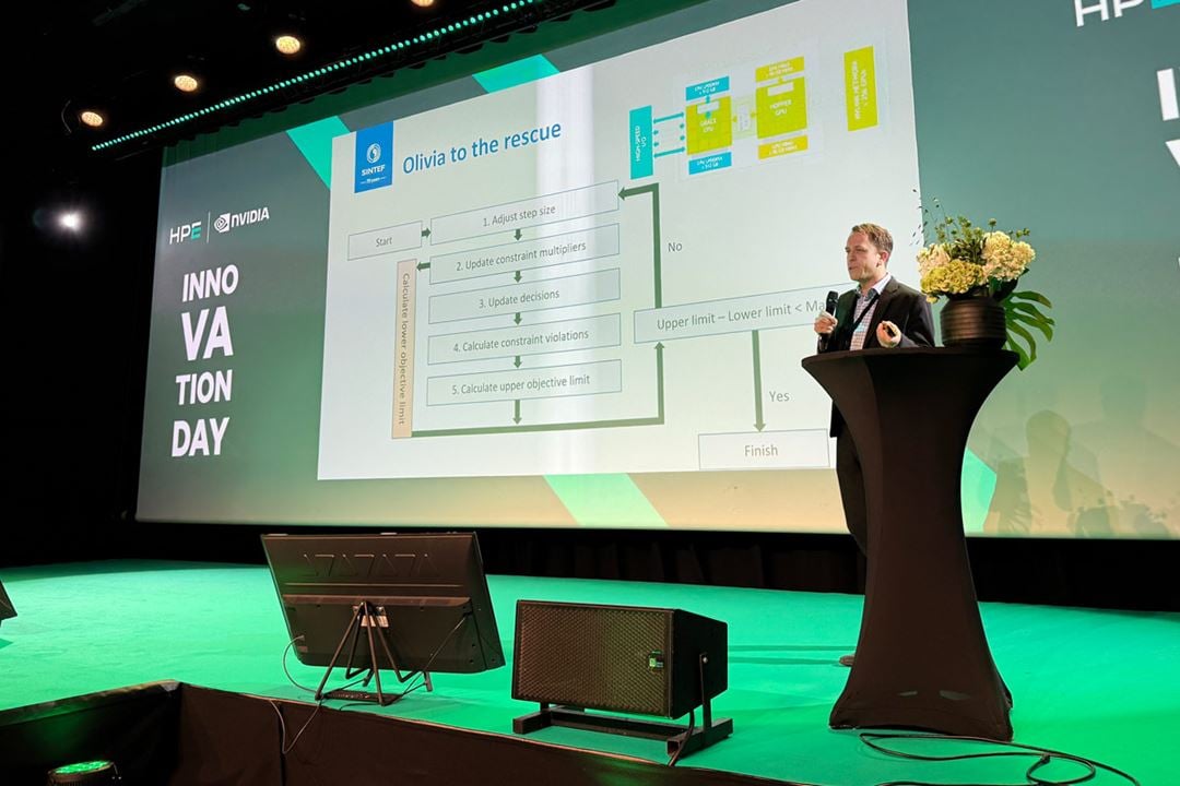 A person is holding a presentation on a stage, in a conference setting, with a screen in the background.