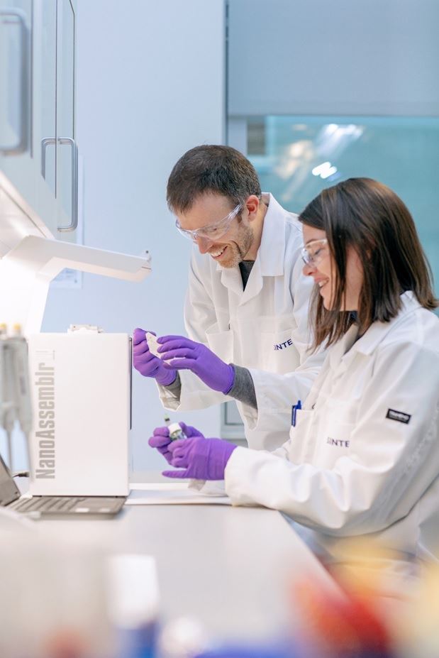 Foto av to personer i hvite frakker som håndterer utstyr på lab
