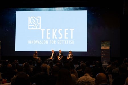 Paneldebatt med fire sittende på scenen foran en skjerm.