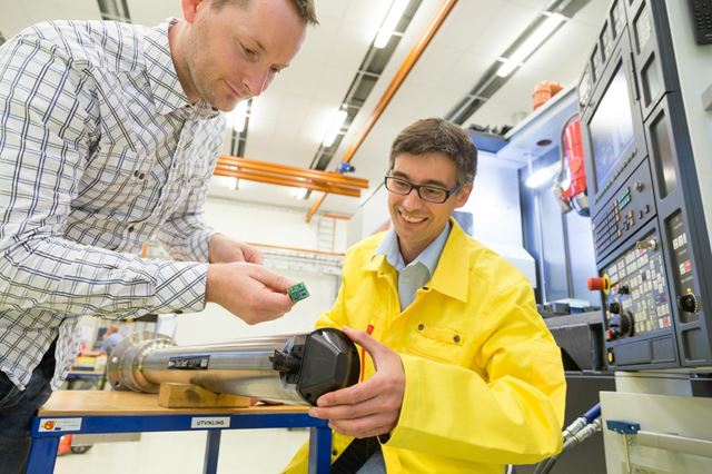 Terje Mugaas fra SINTEF holder sensorpakken som skal monteres på borestangen Tormod Jensen på Sandvik Teeness sitter med. Bak sees en typisk Mori Seiki multitaskmaskin. Foto: SINTEF/Thor Nielsen.
