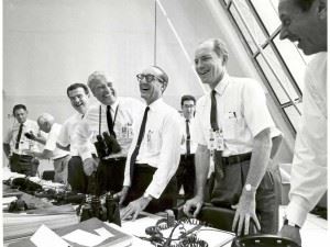 Bilde av gruppe glade menn kledd i hvite skjorter, mørke slips og mørke borte, som jubler over at romskipet Apollo 11 i 1969 har tatt av for historiens første måneferd.