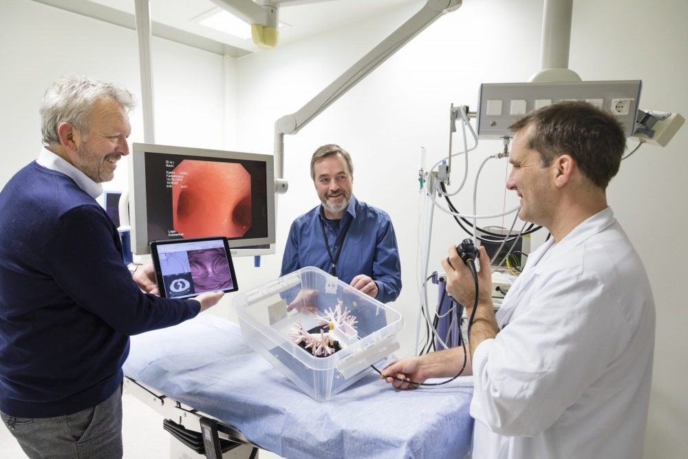 Lungelege Håkon O. Leira fører her et eksisterende bronkoskop inn i en fysisk modell av menneskers lunger. Den store skjermen viser hva undersøkelsesinstrumentet "ser". Teknologene Tor Helge Hansen (til venstre) og Thomas Langø skal sammen sørge for at lungeleger i fremtiden kan styre instrumentet etter tredimensjonale "kart" på et nettbrett. Foto: Thor Nielsen / SINTEF