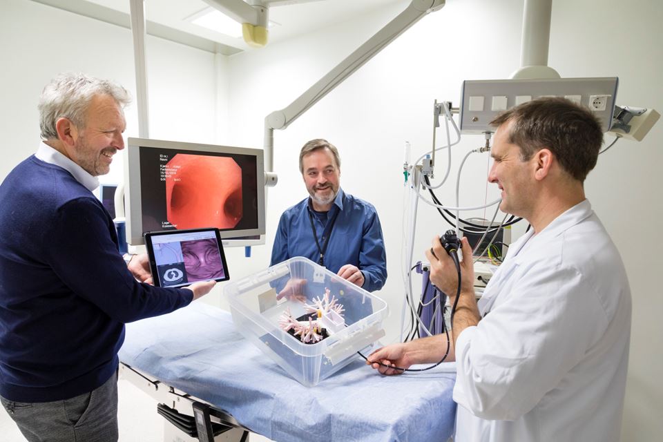 Lungelege Håkon O. Leira fører her et eksisterende bronkoskop inn i en fysisk modell av menneskers lunger. Den store skjermen viser hva undersøkelsesinstrumentet "ser". Teknologene Tor Helge Hansen (til venstre) og Thomas Langø skal sammen sørge for at lungeleger i fremtiden kan styre instrumentet etter tredimensjonale "kart" på et nettbrett. Foto: Thor Nielsen / SINTEF