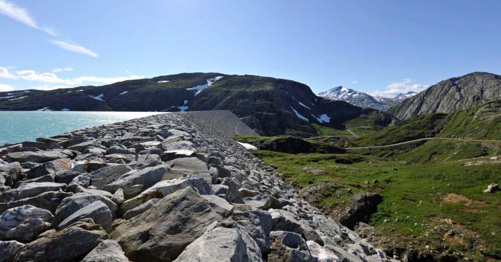 Bildet viser en såkalt steinfyllingsdam som er fylt opp med vann, foran vakkert norsk fjellandskapo.