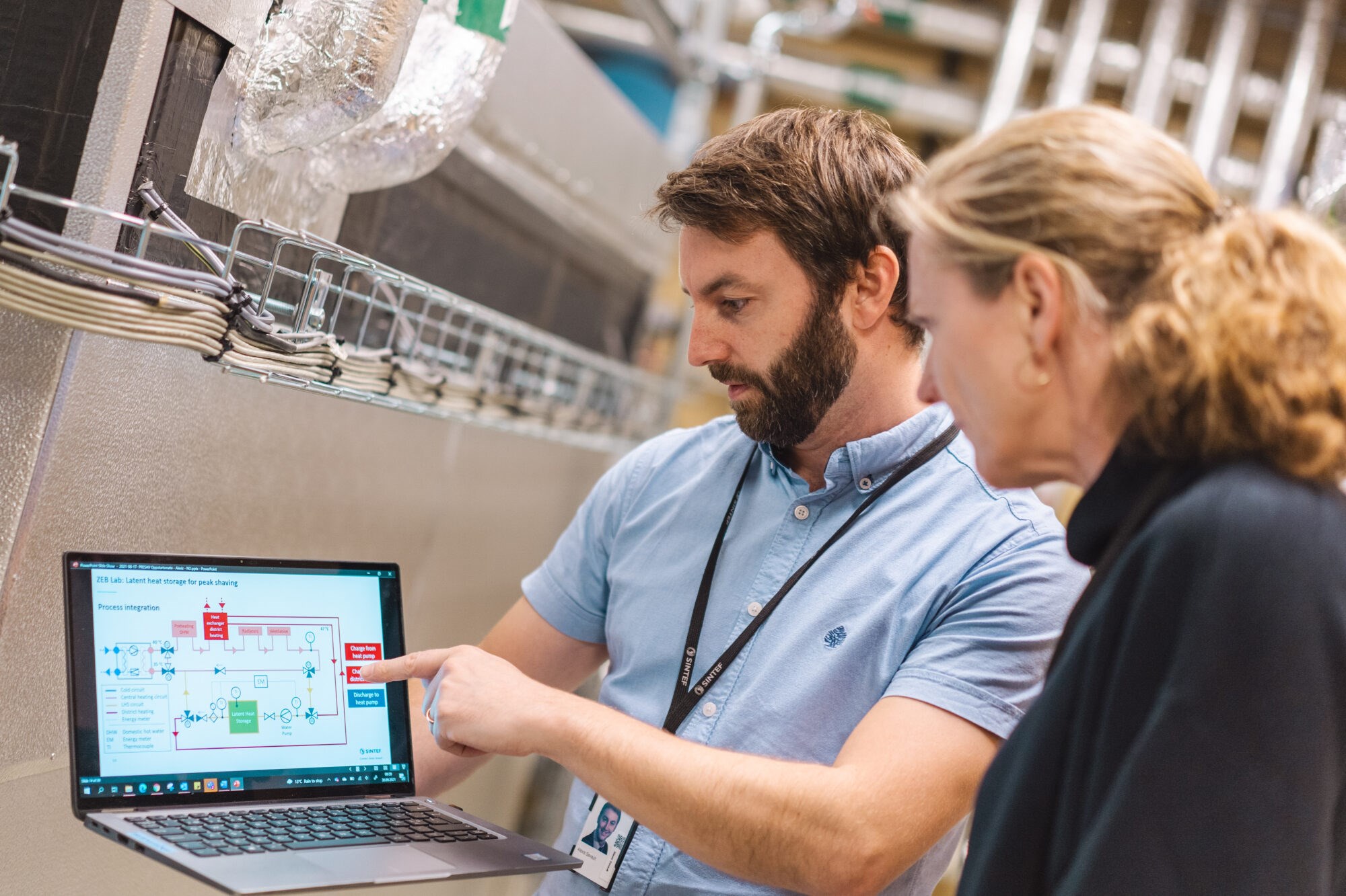 Forskningsleder Alexis Sevault og forsker Fride Vullum-Bruer studerer oppsettet i energisysttemet som er basert på PCM-materiale og varmpepumper. I praksis er dette et biologisk varmelagringssystem - eller batteri, om du vil. Foto: SINTEF/Smidesang&Lyng