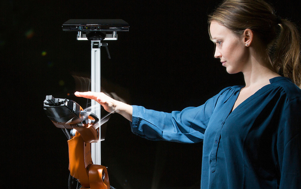 Researcher Marianne Bakken attempting to get close and personal with an orange robot arm – moving in all directions to try to get the robot to collide with her. But it manages to avoid her every time. Photo: Werner Juvik/SINTEF.